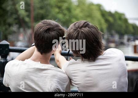 Zwei junge Männer sitzen auf einer Bank und nehmen ein selfie in der Innenstadt von Amsterdam Stockfoto