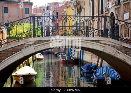 Bezaubernde Brücke und geparkte Boote in einem Wasserkanal in Venedig, Italien Stockfoto