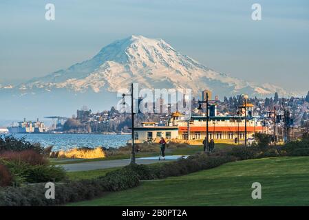 Mt Rainier schwebt über Downtown Tacoma und Beginn der Bucht von Punkt Ruston mit Menschen zu Fuß und Fahrrad Stockfoto