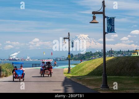 Mt Rainier schwebt über Downtown Tacoma und Beginn der Bucht von Punkt Ruston mit Menschen zu Fuß und Fahrrad Stockfoto