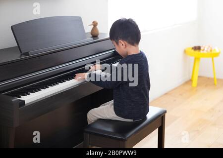 Junge, der dunkelbraunes Klavier im Wohnzimmer spielt Stockfoto