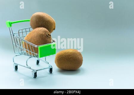 Kiwi in einem kleinen Einkaufswagen auf grauem Hintergrund. Vertriebskonzept. Kopierbereich. Stockfoto