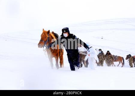 Chinesische Polizisten, Grenzsoldaten und medizinische Arbeiter laufen mit Pferden im Schnee, um lokale Familien zur Prävention des neuen Coronavirus zu besuchen Stockfoto