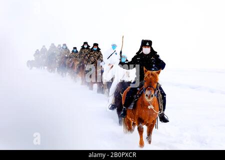 Chinesische Polizisten, Grenzsoldaten und medizinische Arbeiter fahren Pferde im Schnee, um lokale Familien zur Prävention des neuen Coronavirus und p zu besuchen Stockfoto