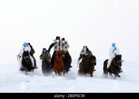 Chinesische Polizisten, Grenzsoldaten und medizinische Arbeiter fahren Pferde im Schnee, um lokale Familien zur Prävention des neuen Coronavirus und p zu besuchen Stockfoto