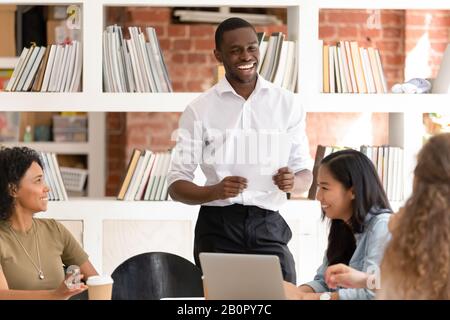 Lachend afroamerikanischer Geschäftsmann mit verschiedenen Mitarbeitergruppen, die Spaß am Treffen haben, freundlicher Business Coach scherzend, glückliches Team, das in lustig verwickelt ist Stockfoto