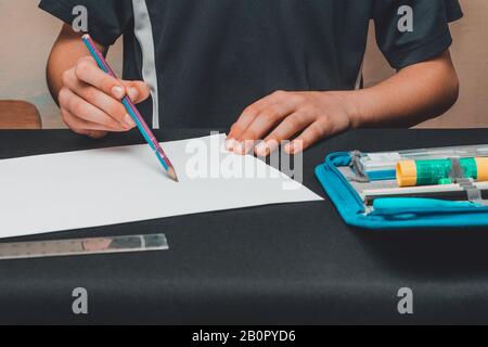 Ein Schuljunge zieht Bleistifte auf weißem Papier. Stockfoto