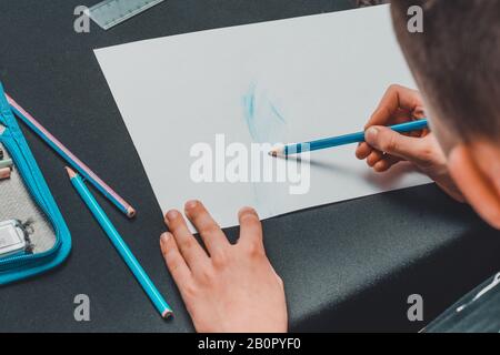 Ein Schuljunge zieht Bleistifte auf weißem Papier. Stockfoto