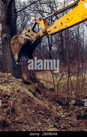 Ein gelber rostiger Industriebagger mit einem Eimer, der auf dem Boden liegt und an einer Baustelle in einem Teichwald den Boden gräbt. Stockfoto