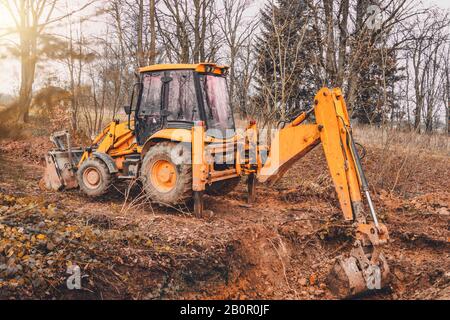 Ein gelber rostiger Industriebagger mit einem Eimer, der auf dem Boden liegt und an einer Baustelle in einem Teichwald den Boden gräbt. Stockfoto