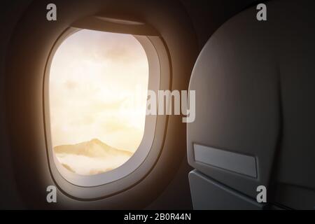 Reise und Reise mit dem Flugzeug: Blick auf schöne Berge und Nebel mit goldenem Sonnenlicht und Linsenflauen, wie man sie durch das Fenster eines Flugzeugs sieht Stockfoto