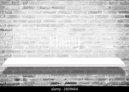 Leeres weißes Ladenregal mit Schatten, Einzelhandelsregal auf Backstein-Vintage-Wandraumhintergrund. Weißes Regal isoliert auf Backstein-Hintergrund. Einlegeboden Stockfoto