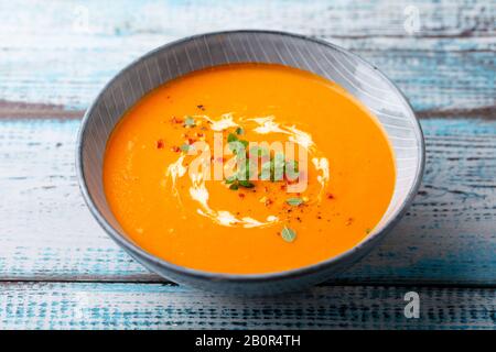 Kürbissuppe mit frischen Kräutern in einer Schüssel. Blauer Holzhintergrund. Nahaufnahme. Stockfoto