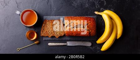 Banane, Kokosbrot, Kuchen mit Teetasse auf Schieferplatten. Hintergrund aus dunklem Stein. Draufsicht. Stockfoto