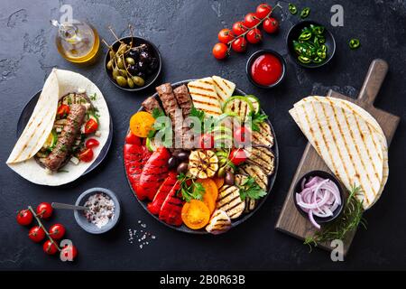 Gegrilltes Fleischkebabs, Gemüse auf schwarzem Teller mit Tortillas, Fladenbrot. Hintergrund aus Schieferstein. Draufsicht Stockfoto