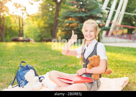 Fröhliche Mädchen-Studentin lächelt. Schulmädchen in Uniform zeigt fröhlich Geste, alles ist gut mit den Daumen nach oben. Tutorial Stockfoto