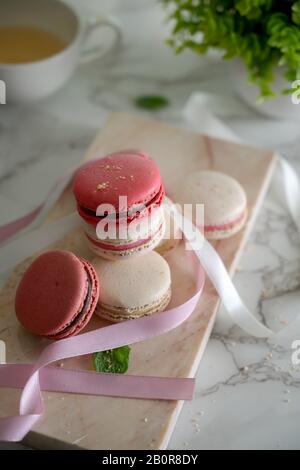 3/4-Schuss Farbenfroher Pastellmakarone auf Marmortablett mit Band, Teetasse und Baumkanne auf Marmortisch Stockfoto