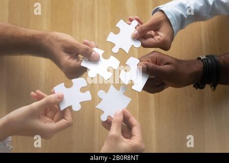 Hände verschiedener Teammitglieder, die Puzzle auf dem Schreibtisch zusammenstellen, afroamerikanische und kaukasische Kollegen finden Lösung, arbeiten an projec Stockfoto