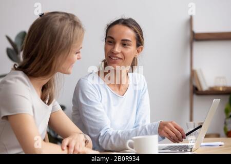 Lächelnde Geschäftsfrau mit Kollegen, die gemeinsam an einem Computerprojekt arbeiten, mit Laptop, Blick auf den Bildschirm, Mentor, der die Aufgabe erklärt und bei Corpo hilft Stockfoto