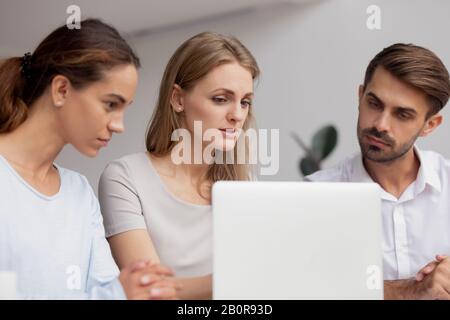 Seriöse, fokussierte Geschäftsfrau, Mentorin, die Mitarbeiter im Büro schult, erklärt Online-Projekt, hilft Auszubildenden mit neuer Software, Kollegen arbeiten zusammen Stockfoto