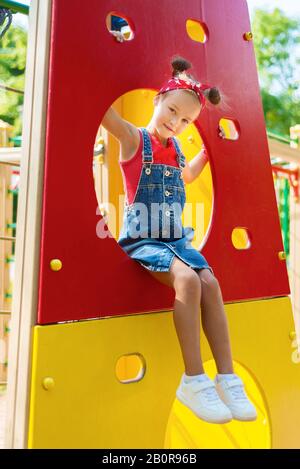 Porträt der kleinen, hübschen Mädchen in Jeans Overall mit rotem Hemd und Taschentuch. Kind auf dem Spielplatz Stockfoto