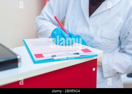 Arzt in blauen Gummihandschuhen füllt einen Fragebogen und Patientendaten aus Stockfoto