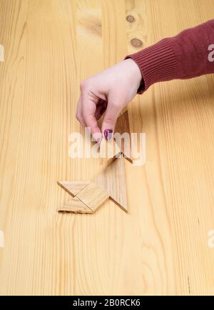 Mädchen sammelt auf einem Holztisch ein Holz-Tangram-Puzzle. Chinesisches Tangram-Puzzle. Puzzle-Konzept. Stockfoto