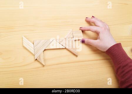 Mädchen sammelt auf einem Holztisch ein Holz-Tangram-Puzzle. Chinesisches Tangram-Puzzle. Puzzle-Konzept. Stockfoto