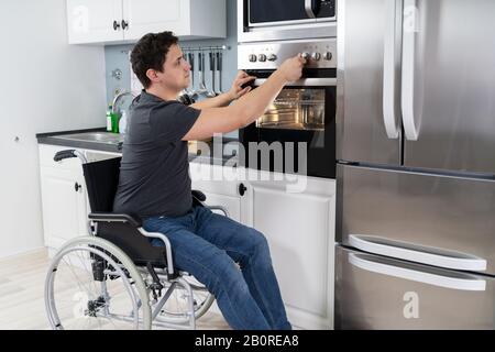 Behindertengerechter Mann Mit Mikrowellenofen Zum Backen In Der Küche Stockfoto