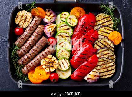 Gegrilltes Fleischkebab und Gemüse in der Grillpfanne. Hintergrund aus schwarzem Stein. Draufsicht. Stockfoto