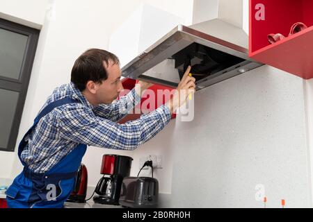 Nahaufnahme Eines Jungen Elektrofachelektrikers, der den Kitchen Extractor instand setzen soll Stockfoto