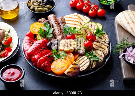 Gegrilltes Fleischkebabs, Gemüse auf schwarzem Teller mit Tortillas, Fladenbrot. Hintergrund aus Schieferstein. Nahaufnahme. Stockfoto