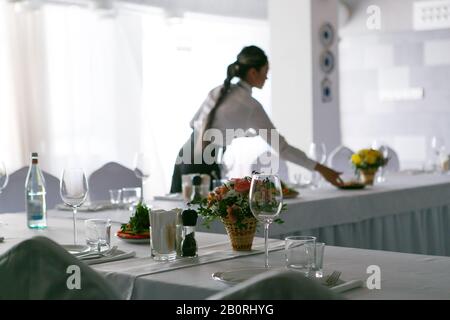 Die Kellnerin mit langem Ferkel serviert den Banketttisch im Restaurant Stockfoto