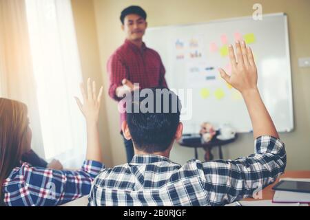 Eine Gruppe junger Leute, die gemeinsam auf der Konferenz sitzen, während Leute, die Hand erheben, Fragen stellen. Stockfoto