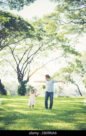 Kleines Mädchen, das die Hände hält, während ihr Vater im Park spazieren ging, Glückszeit. Stockfoto