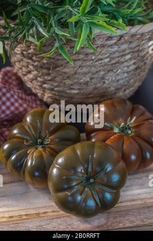Schwarze Tomaten. Drei Kumato Tomaten auf einem Holzbrett. Bild Auffüllen. Stockfoto