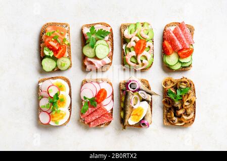 Verschiedene Sandwiches mit Fleisch, Gemüse und Seefahrt. Auswahl an offenen Sandwiches auf hellem Steingrund. Leckerer, gesunder Snack. Draufsicht, flach l. Stockfoto