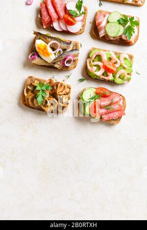 Verschiedene Sandwiches mit Fleisch, Gemüse und Seefahrt. Auswahl offener Sandwiches auf hellem Steingrund mit freiem Textbereich. Leckere gesunde sn Stockfoto