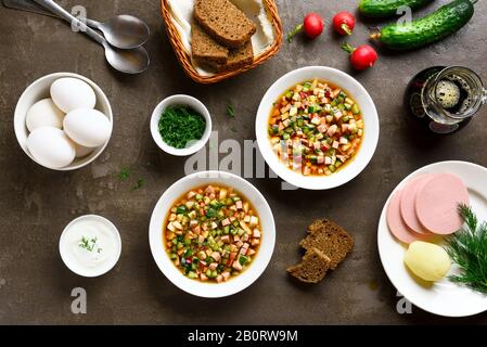 Traditionelle kalte russische Okroschka-Suppe und Zutaten über braunem Steingrund. Leckeres Sommergericht zum Abendessen. Draufsicht, flacher Lay Stockfoto