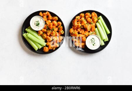 Büffelflügel aus Blumenkohl mit Sellerie und Sauce auf Platte über weißem Steinhintergrund mit freiem Textraum. Gesundes Essen, pflanzliches Lebensmittelkonzept. T Stockfoto