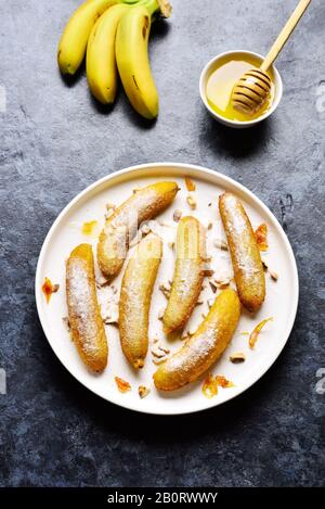 Frittierte Bananen auf weißem Teller über blauem Steingrund. Leckeres Dessert aus panfrittierten Bananen im asiatischen Stil. Stockfoto