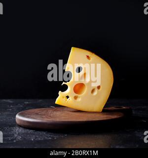 Käse-Maasdamm-Stück auf einer Schneideplatte. Hintergrund aus schwarzem Stein. Kopierbereich. Stockfoto