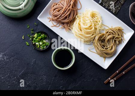 Sortiment japanischer Soba Nudeln mit Sauce und Beilagen. Schwarzer Schiefer Hintergrund. Ansicht von oben. Stockfoto