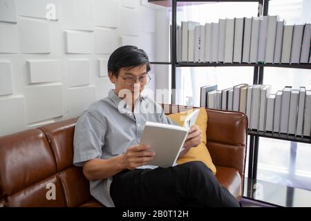Senior Asian man spielt Tablet und Video Call auf dem Sofa im Wohnzimmer zu Hause Portrait des asiatischen älteren Mannes ist Entspannend und Glücklich Mit dem Spielen von TA Stockfoto