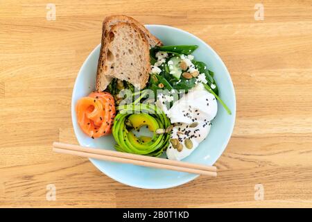 Gesunde Ernährung. Salat mit Fisch: Lachs, Hefefreies Brot, pochiertes Ei, Avocado, Spinat, chio-Samen, Sesamsamen, Kürbissamen, Hüttenkäse. Essstäbchen. Holzhintergrund. Stockfoto