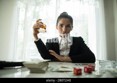 Geschäftsmann, der in einer Business Center-Bar sitzt und Zigarre raucht und Whisky und Geld auf dem Tisch trinkt. Stockfoto