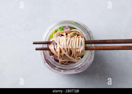 Soba Nudeln Salat, Suppe mit Gemüse, Tofu und Huhn in Gläsern. Grauer Hintergrund. Close Up. Ansicht von oben. Stockfoto