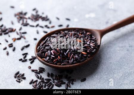 Schwarzer Wildreis in einem Holzlöffel. Grauer Steinhintergrund. Nahaufnahme. Stockfoto