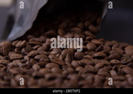 Kaffeebohnen verschütten sich aus einer schwarzen Packung. Stockfoto