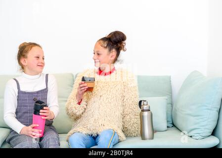 Teenager-Mädchen sprechen, lachen und trinken Tee aus wiederverwendbaren Tassen.Jugendliche, die versuchen, die Welt zu verändern, indem sie Umweltbelange in ihre eigenen Hände nehmen.Nullabfälle und schwaches Wohnkonzept. Stockfoto